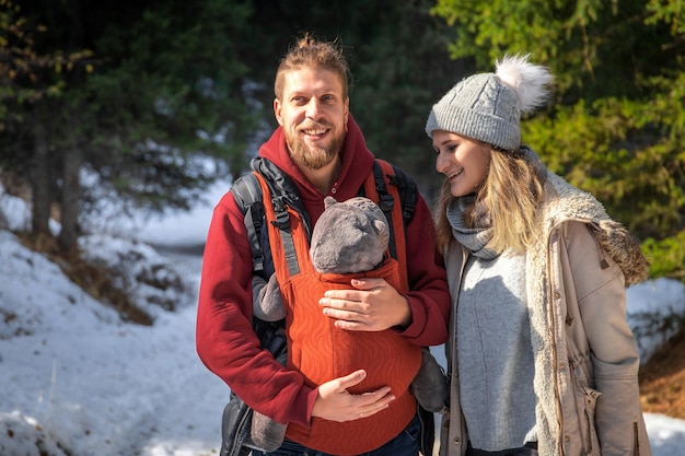 Balade en forêt d'hiver avec la famille et leur bébé dans un porte-bébé ergonomique