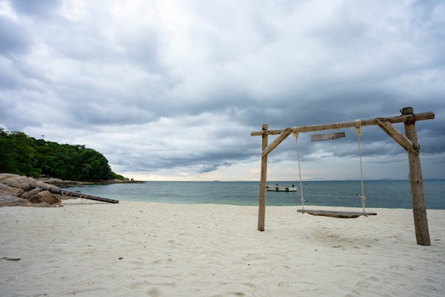 Photo balançoire en bois suspendu à une branche d'arbre à la mer turquoise sur la plage en face de la mer