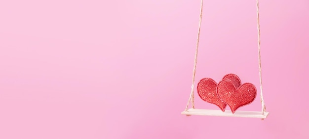 Une balançoire avec deux coeurs sur fond rose Bannière créative pour le 14 février Copier l'espace