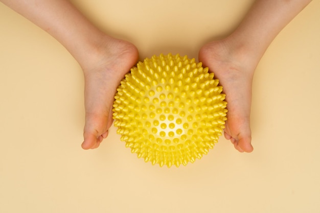 Balle d'équilibrage à aiguille jaune pour le massage et la physiothérapie sur fond beige avec l'image d'un pied d'enfant le concept de prévention et de traitement de l'hallux valgus