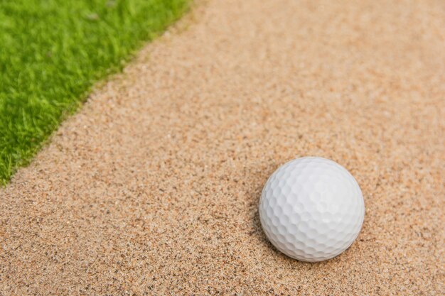 Balle de golf blanche dans le bunker de sable sur le terrain de golf