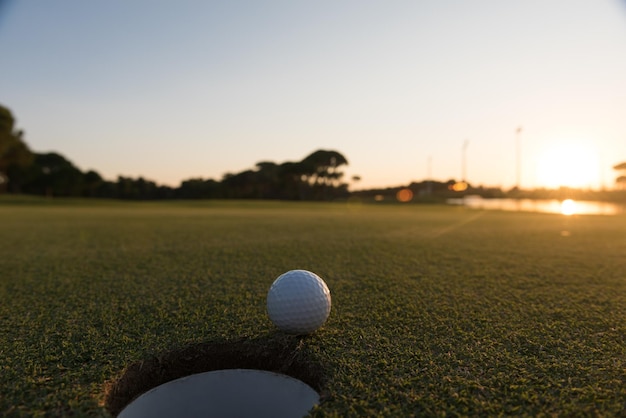 balle de golf sur le bord du trou du parcours représentant la réussite et le succès du concept d'entreprise, beau coucher de soleil en arrière-plan