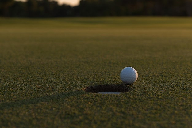 balle de golf sur le bord du trou du parcours représentant la réussite et le succès du concept d'entreprise, beau coucher de soleil en arrière-plan