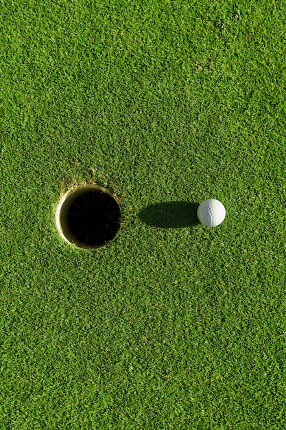 Balle de golf sur l'herbe verte avec trou et lumière du soleil