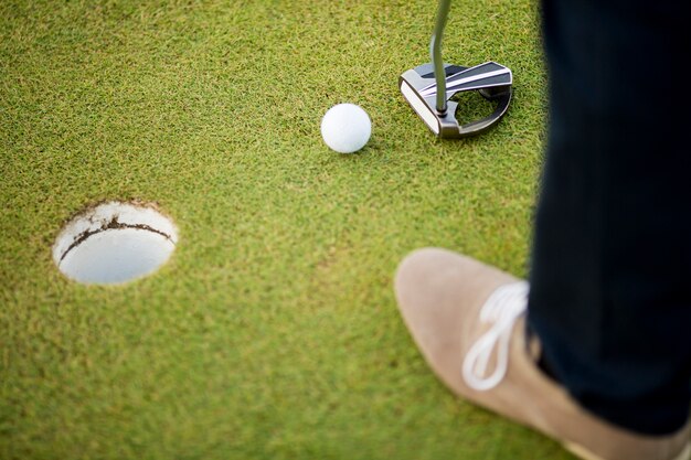 Balle de golf, putter et jambes de garçon sur vert