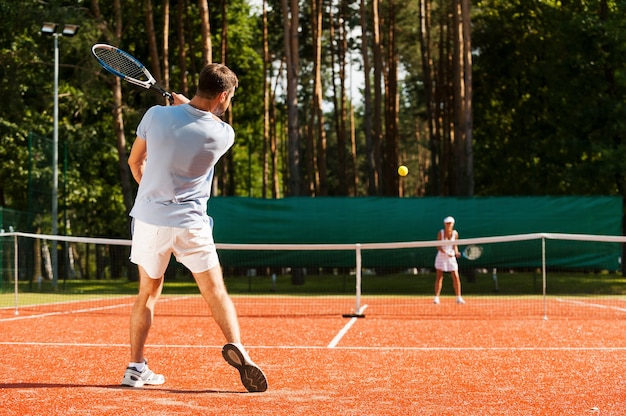 Balle de match. Toute la longueur de l'homme et de la femme jouant au tennis sur un court de tennis