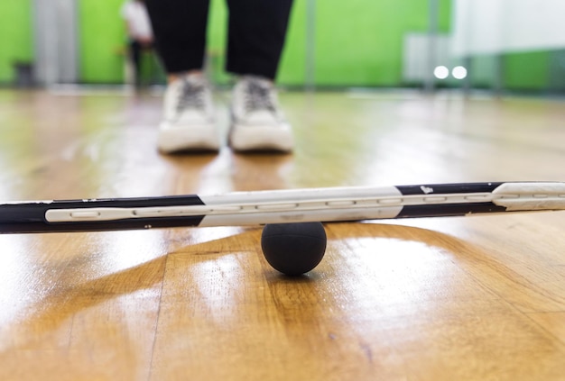 Une balle de squash noire se trouve sous une raquette de tennis sur un parquet photo horizontale