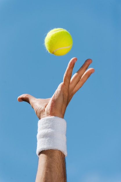 Balle de tennis au service. Close-up of male hand in bracelet lançant une balle de tennis contre le ciel bleu