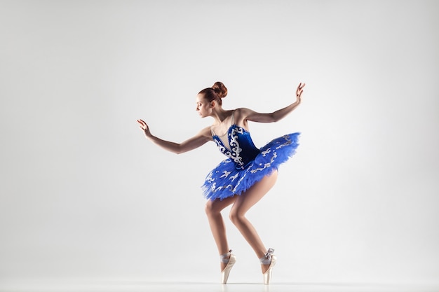 Ballerine attrayante avec chignon recueilli des cheveux vêtue d'une robe bleue et de chaussons de pointe se produisant en studio blanc. intérieur, tourné en studio.