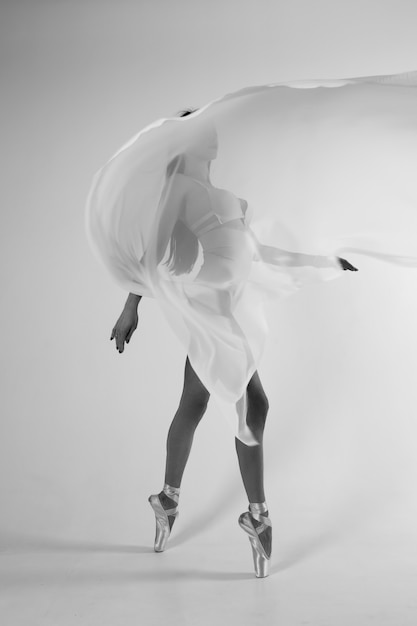 Ballerine en corps sur un mur blanc avec un tissu blanc volant. Vidéo en noir et blanc.