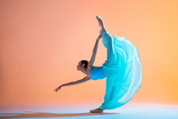 Ballerine dans une robe bleu clair danse sur un fond coloré avec rétro-éclairage rose