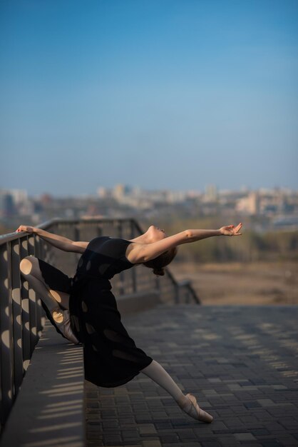 Ballerine dans un tutu posant près de la clôture Belle jeune femme en robe noire et danse de pointe à l'extérieur Superbe ballerine démontre un étirement incroyable
