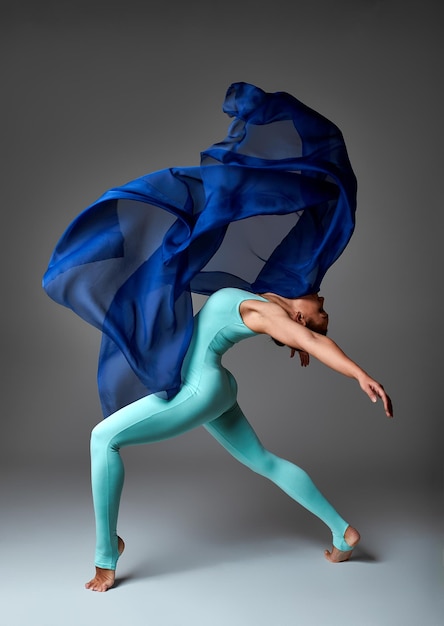 Ballerine dansant avec une danseuse de ballet moderne en tissu de soie en tissu ondulant flottant sur fond gris