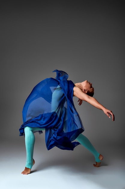 Ballerine dansant avec une danseuse de ballet moderne en tissu de soie en tissu ondulant flottant sur fond gris