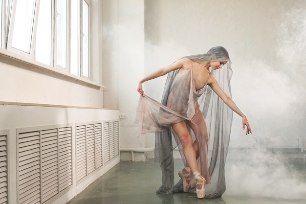 Photo ballerine danse dans une longue robe et sa tête est recouverte d'un voile gris, avec de la fumée en arrière-plan