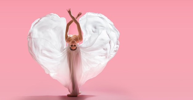 Ballerine élégante en chaussons de pointe dansant dans une longue jupe blanche se développant en forme de coeur sur fond rose