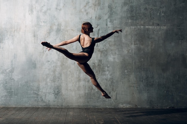 Photo ballerine saut pas. belle jeune femme danseuse de ballet, vêtue d'une tenue professionnelle, de chaussons de pointe et d'un corps noir.