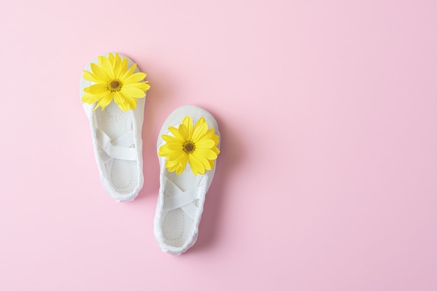 Ballerines blanches à fleurs jaunes sur une table rose avec espace de copie.