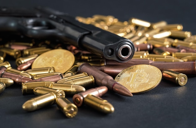 Balles de pistolet en bronze et en laiton éparpillées sur une table sombre, canon de pistolet noir, pièces de monnaie dorées à proximité - utilisation illégale de crypto-monnaie pour acheter un concept d'arme