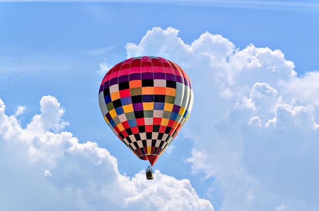 Ballon à air chaud coloré survolant un ciel bleu avec des nuages blancs