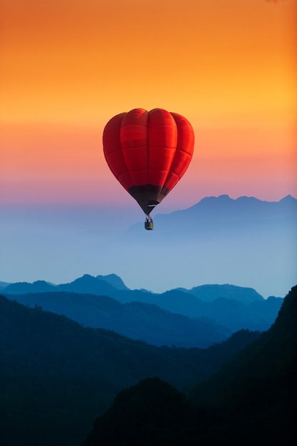 Ballon à air chaud rouge unique survolant les montagnes bleues