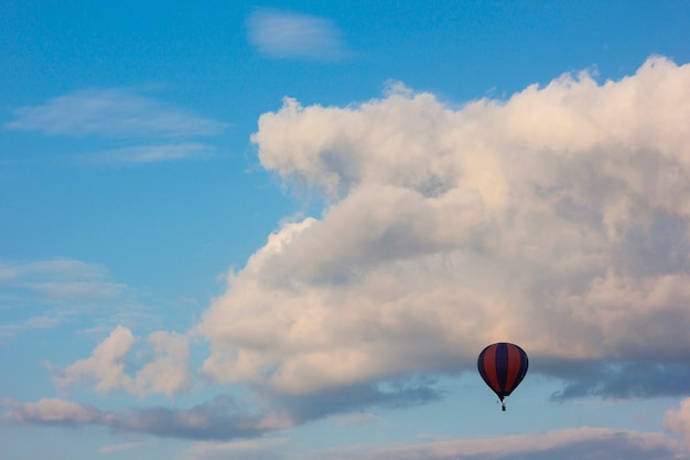 Ballon à air solitaire volant devant des nuages gonflés blancs