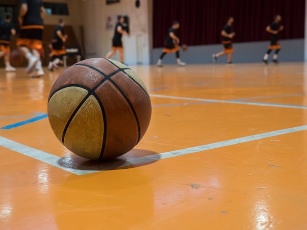 Ballon de basket sur le terrain avec ligne de lancer franc, joueurs flous