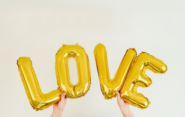 Ballon doré gonflable en feuille d'inscription LOVE dans les mains sur le fond blanc. Roman d'amour