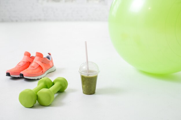 Ballon de fitness, haltères et verre avec kiwi frais sur le sol dans la salle blanche