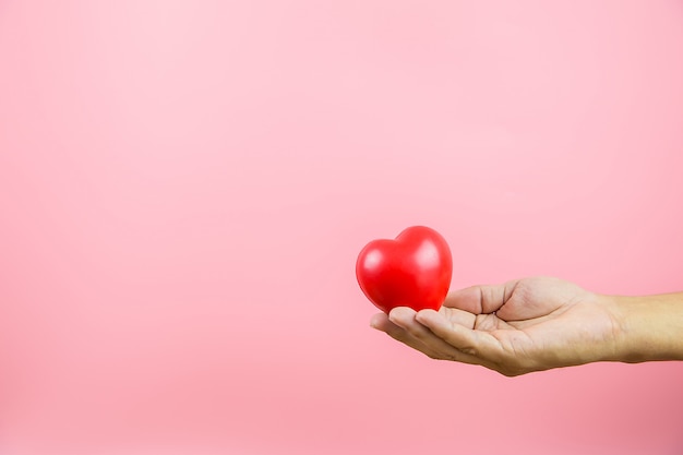 Un ballon en forme de coeur rouge dans sa main sur un fond rose concept de la Saint-Valentin 14 février amour et bonne journée.