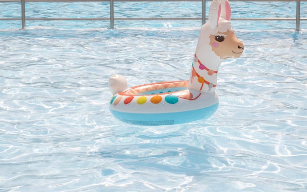 Le ballon gonflable de natation d'anneau de lama flotte sur la piscine d'eau. beaucoup d'enfants jouent dans le dos