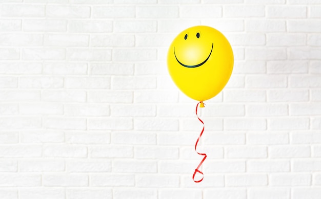 Ballon jaune avec sourire volant contre un mur blanc Espace de copie