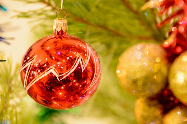 Ballon de Noël rouge sur un arbre de Noël sur fond de guirlandes brillantes. Boule rouge entourée de branches de l'arbre de Noël. Notion de Noël.