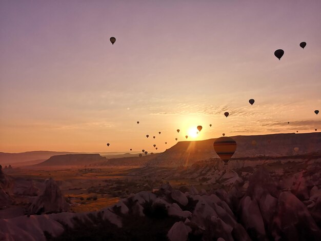 Des ballons à air chaud volant au-dessus du paysage contre le ciel au coucher du soleil