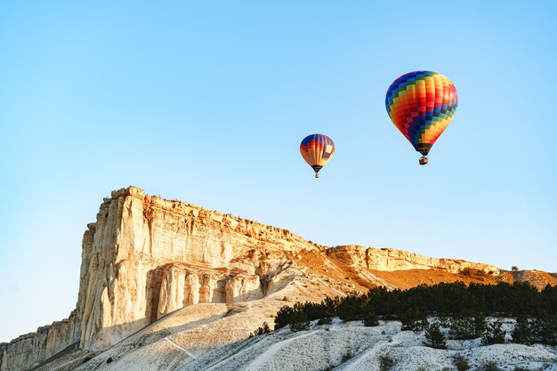 Ballons à air colorés volant dans un ciel clair près d'énormes montagnes blanches aux beaux jours