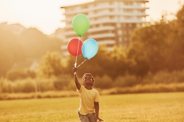 Avec des ballons dans les mains, un enfant afro-américain s'amuse sur le terrain pendant la journée d'été