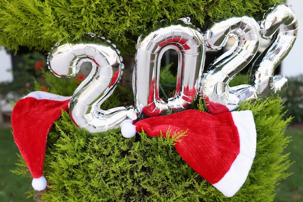 Ballons d'hélium argentés avec des nombres accrochés à un arbre de Noël près de chapeaux rouges en gros plan du père noël ...