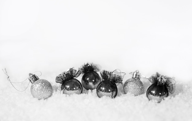 Ballons de Noël argentés et noirs et neige sur fond blanc.