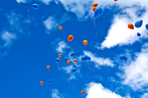 Ballons oranges et bleus contre le ciel et les nuages blancs