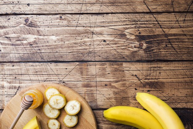 Banane et banane coupée en morceaux avec du miel sur une table en bois,