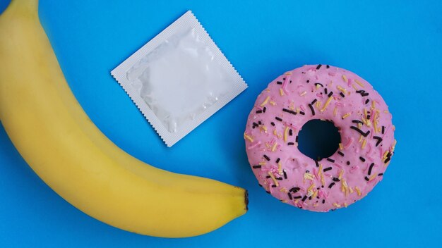 Banane, beignet et préservatif. Idée de sexe. Image lumineuse sur fond bleu. Le concept de santé et de sexe protégé