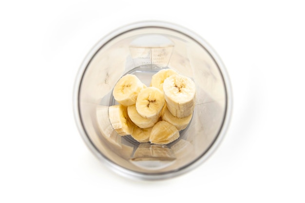 Banane coupée en tranches dans un récipient transparent sur fond blanc Vue de dessus mise à plat