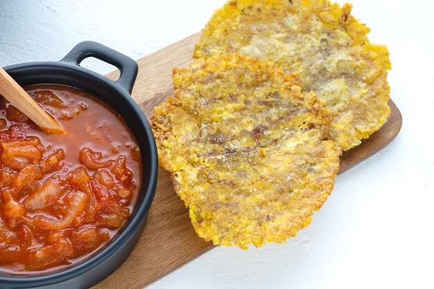 Banane frite avec sauce tomate dans une casserole sombre sur une table de cuisine avec une surface blanche. Concept de cuisine latine.