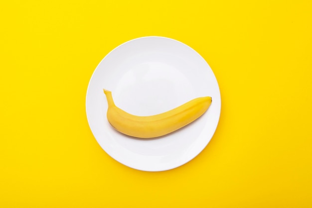 Banane jaune vif sur plaque en céramique blanche Composition minimale créative