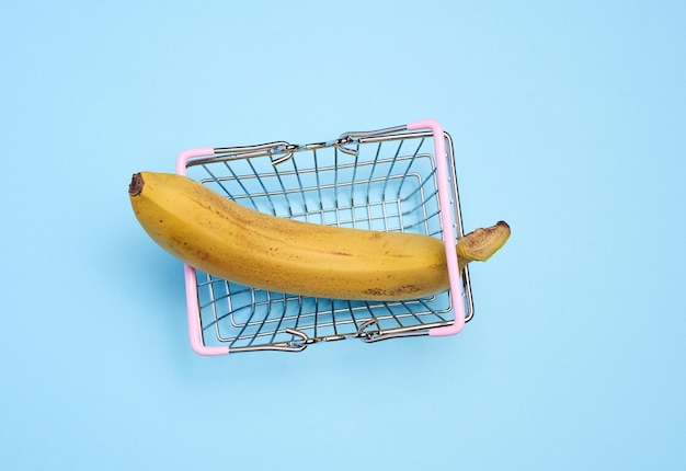 Une banane mûre dans un panier miniature sur fond bleu représentant le concept de vente de fruits et légumes