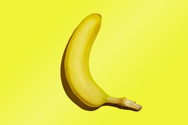 Une banane mûre entière isolée sur un fond dégradé jaune.