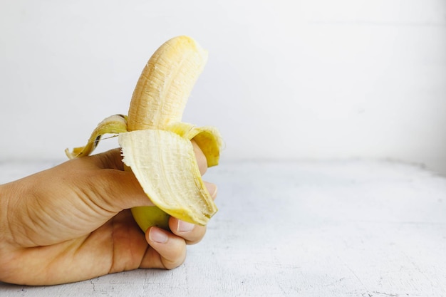 Banane ouverte à la main sur une table en bois blanche