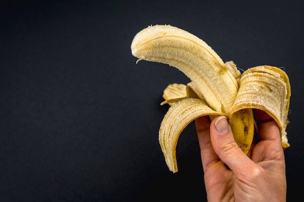 Une banane pelée dans la main d'une femme sur fond noir