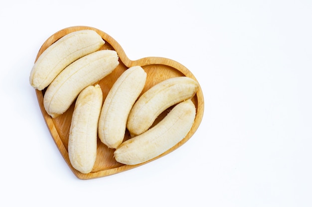 Banane pelée sur plaque en forme de coeur sur fond blanc.