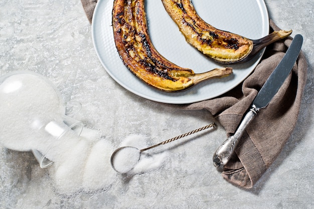 Bananes cuites au four avec du miel sur une assiette grise.